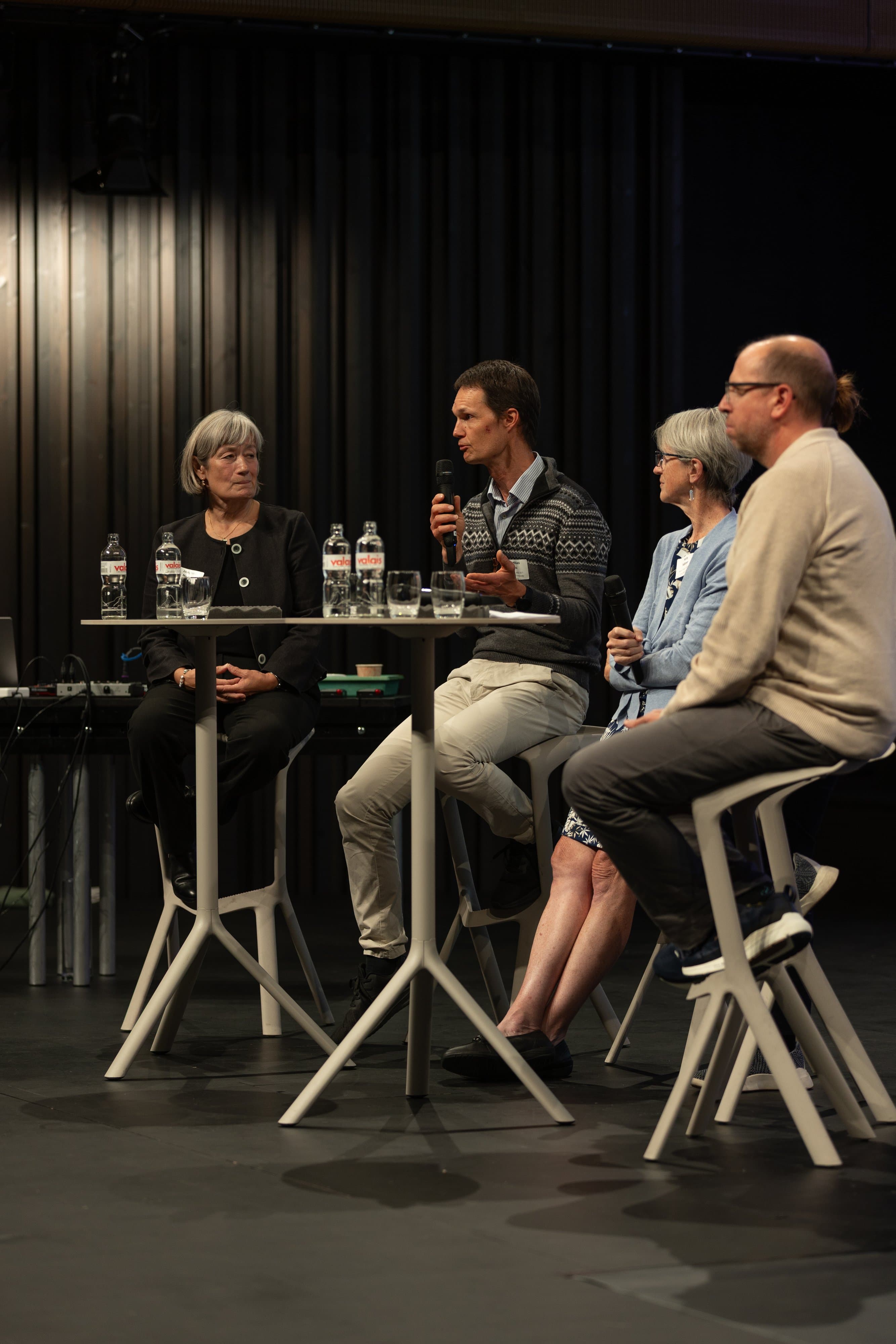 Table ronde de quatre intervenants assis sur des tabourets hauts, sur une scène sombre